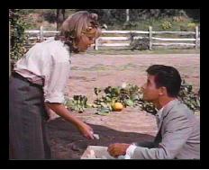 Nancy dressed in trousers with her hair in pins, runs out the door and into a handsome young stranger
